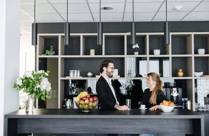 Zwei Menschen stehen neben Kaffeemaschine, trinken Kaffee und Wasser, unterhalten