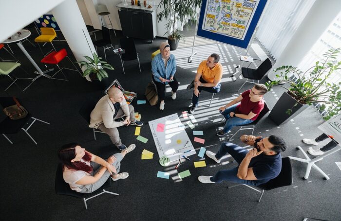 Sechs Menschen sitzen im Kreis und diskutieren miteinander, auf Boden liegt einen Flipchart mit farbige kleine Zettel