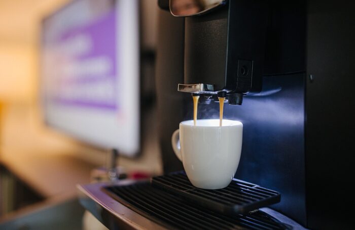 Eine schwarze Kaffeemaschine im Betrieb: Kaffee fließt in eine weiße Tasse ein.