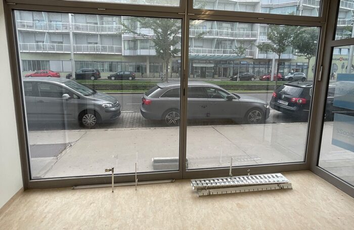 Ein Raum von innen mit großer Glasfront. Draußen verläuft eine breite Straße, an der Autos parken.